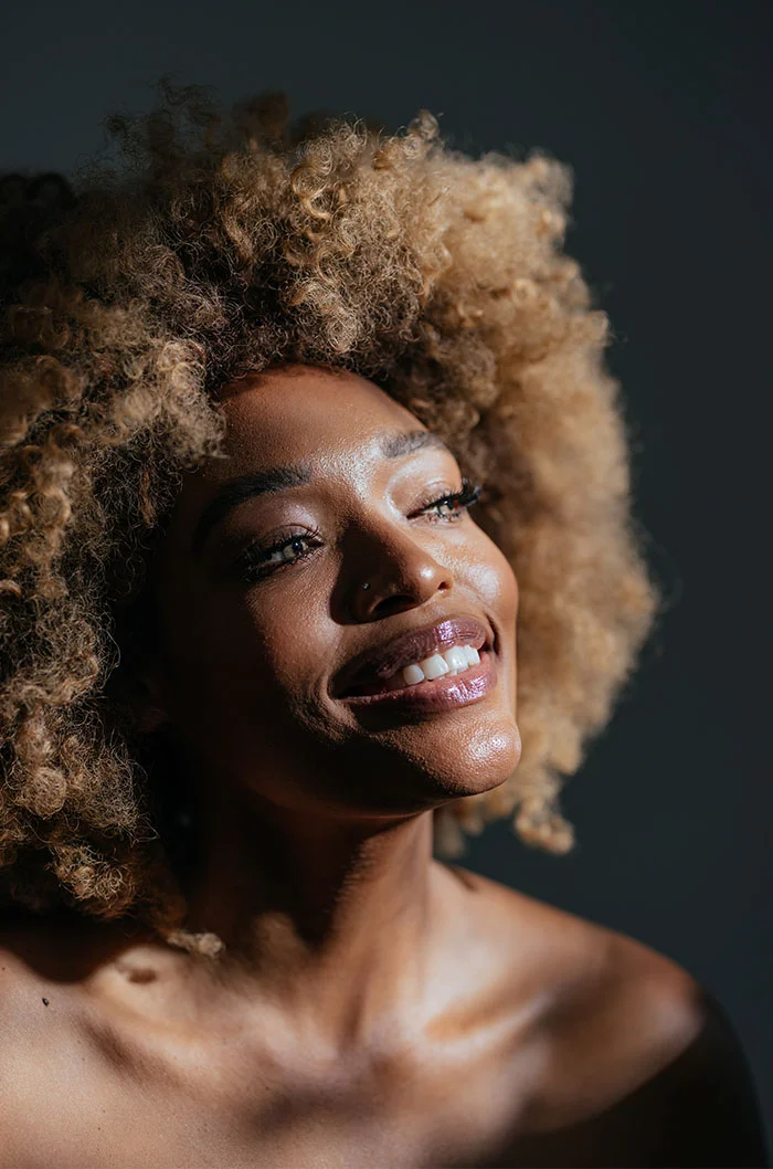 A woman with a radiant smile, her curly blonde hair catching the light, creating a warm and joyful atmosphere - Botox and Wrinkle Relaxers in Marietta, GA