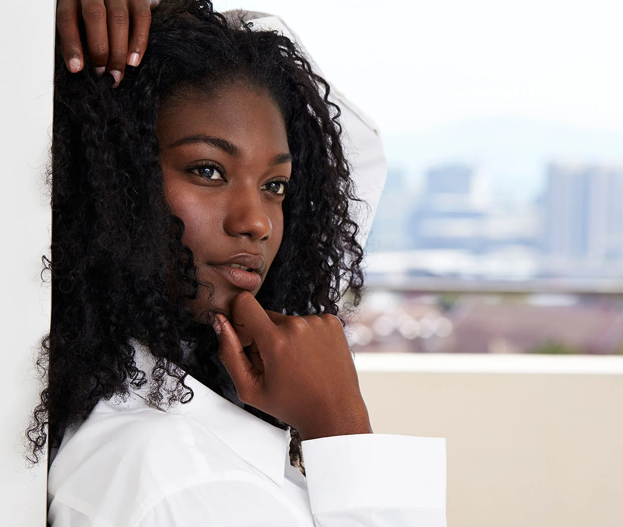 A woman with curly dark hair, leaning against a wall - Laser Skin Resurfacing at Eleve Plastic Surgery
